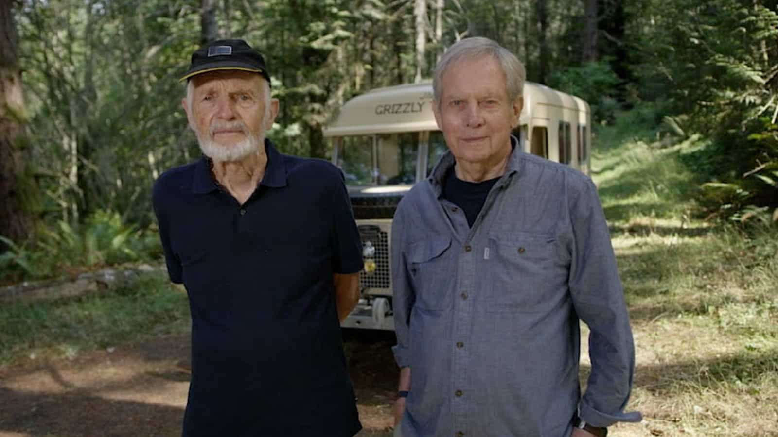Two people standing in front of Land Rover Defender in a forest